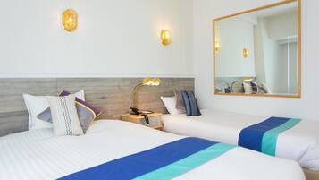 Habitación de hotel con dos camas, una mesita de noche, una lámpara, un espejo y apliques en la pared.