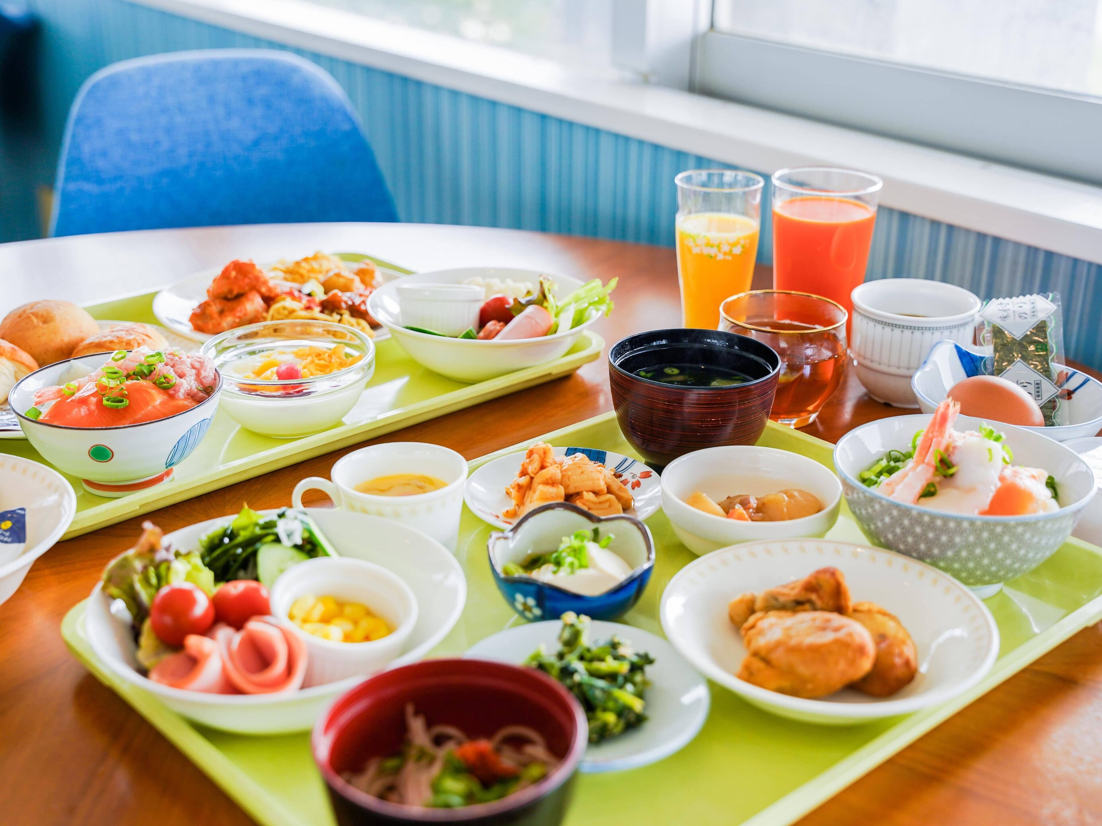 Una mesa servida con diversos platos, entre ellos sopas en cuencos, comida en platos y vasos de jugo, en una habitación con una ventana y una silla azul al fondo.