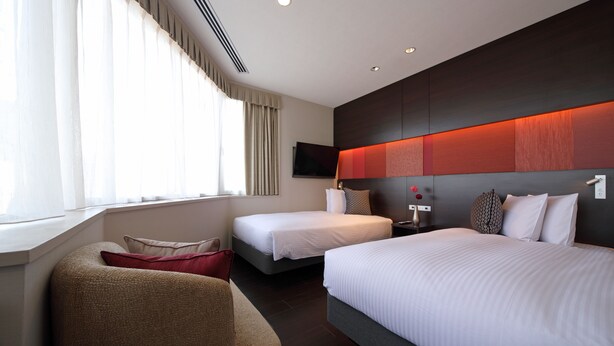 Een hotelkamer met twee bedden, een bank, een televisie en een raam met gordijnen.