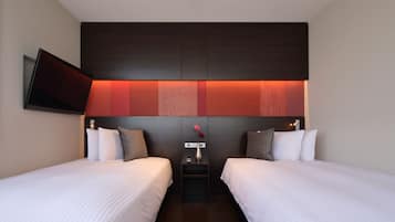 Habitación de hotel con dos camas, un televisor de pantalla plana montado en la pared, una mesita de noche con un jarrón y un cabecero moderno con iluminación integrada.