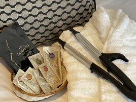 Un cesto con prodotti per la cura della pelle, una piastra per capelli e una borsa nera con l'etichetta 'Labeuna sheet mask' su un letto con un cuscino fantasia.