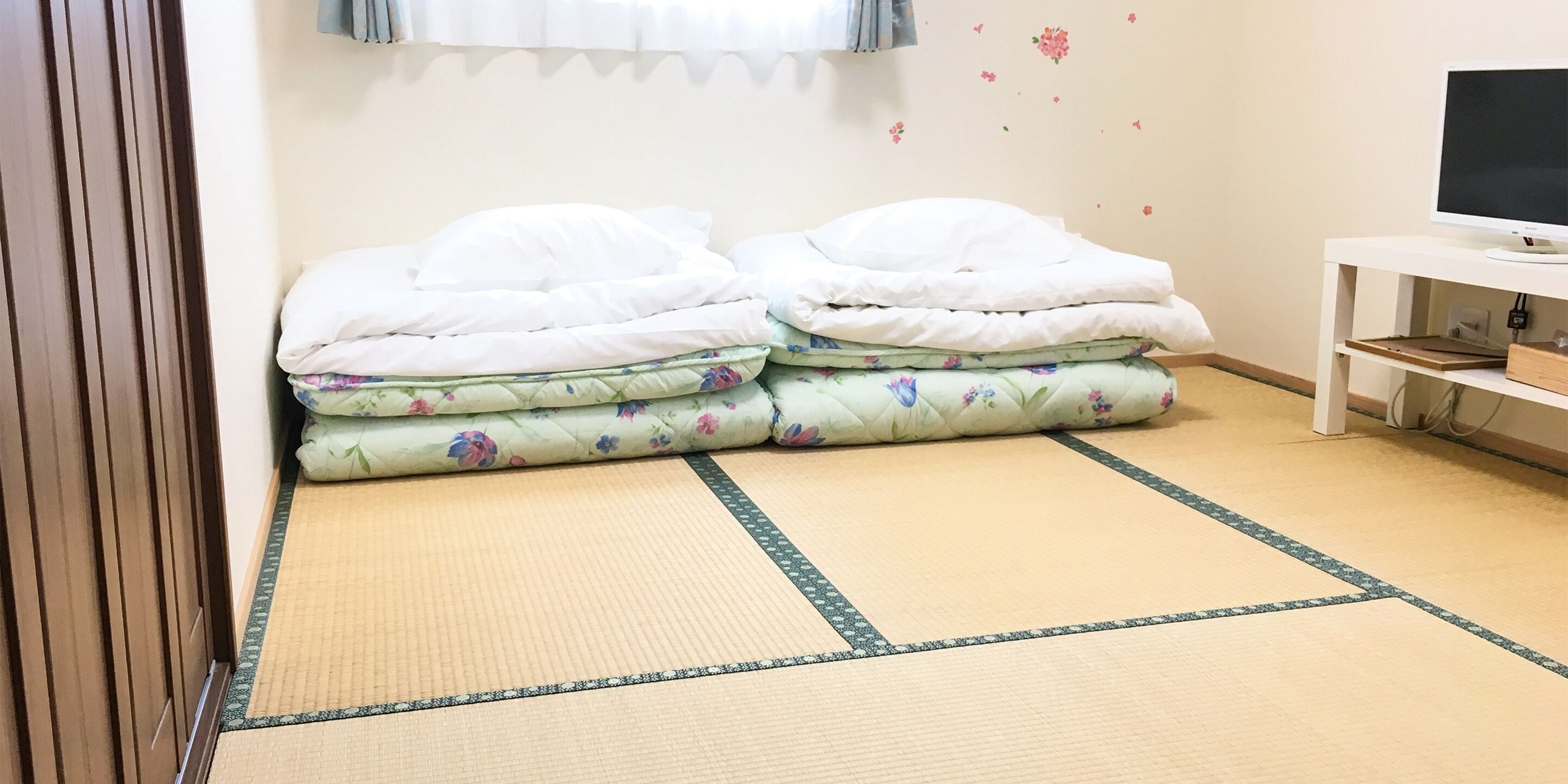 Una habitación con una cama, un televisor sobre un mueble bajo y una pared decorada con diseños florales.