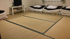 Una habitación con esteras de tatami, un televisor sobre un soporte blanco y ropa de cama ordenada.