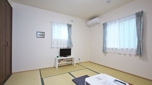 Una habitación con suelo de tatami, un televisor sobre un pedestal blanco y una mesa con documentos y un control remoto.