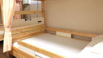 Una cama litera de madera con un escritorio extraíble y una ventana con cortinas.
