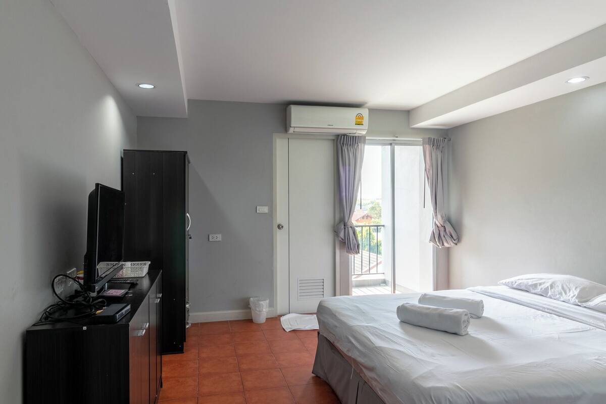 Une chambre d’hôtel équipée d’un lit, d’une télévision, d’une armoire, d’un appareil de climatisation et d’une fenêtre avec des rideaux.