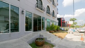 Een modern gebouw met grote ramen, een trap die naar de ingang leidt, en een kleine tuin met een bloembak.