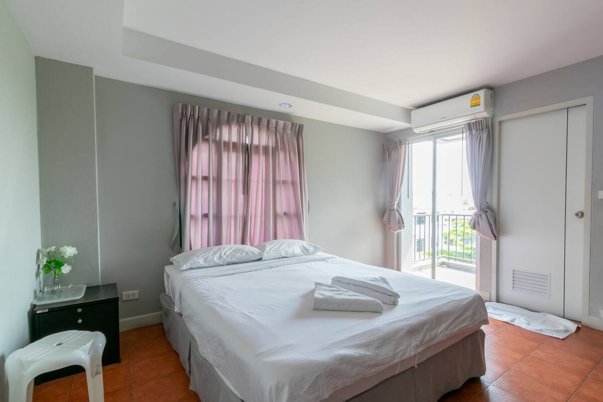 Une chambre à coucher avec un lit, une table de chevet, une petite table et une fenêtre avec des rideaux.