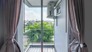 Een balkon met uitzicht op een stadsgezicht, een raam met zonwering en een elektrische schakelkast aan de muur.