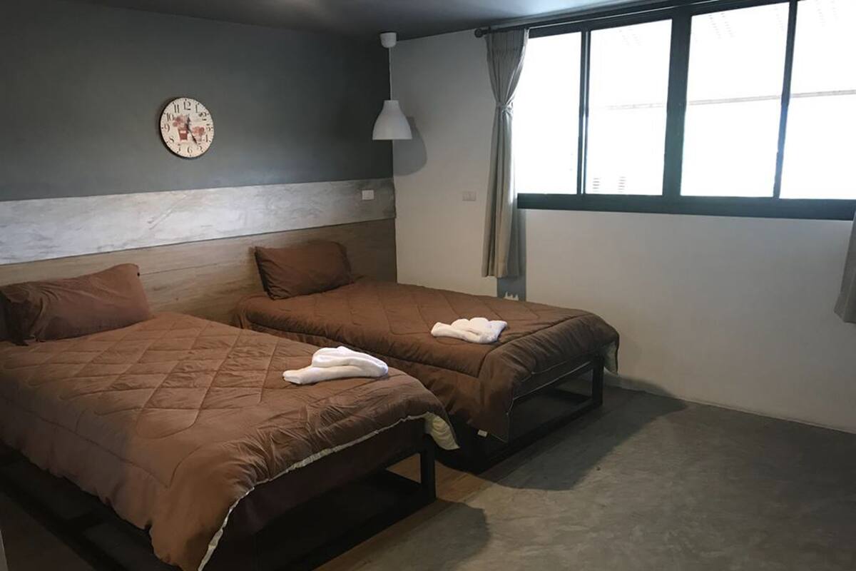 Een kamer met twee bedden, een klok aan de muur, een raam met gordijnen en een lamp.