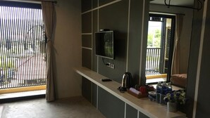 Habitación compacta con televisión, una pequeña kitchenette, ventana con persianas y vistas al balcón.