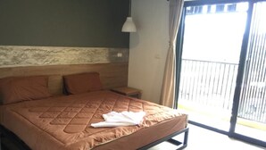 Una cama individual con colcha marrón, una mesita de noche, una lámpara y vistas a un balcón.