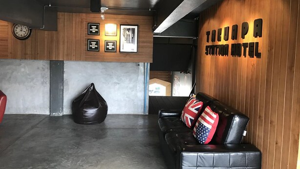 Un lobby de hotel moderno con una pared de madera, un sofá de cuero negro con banderas británicas, un asiento informal de tela negra y un reloj a la izquierda.