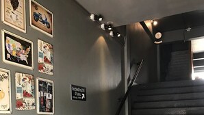 Una escalera con barandilla de metal, una pared decorada con cuadros de temática cafetera y una mesita con una planta en maceta.