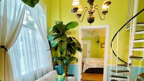 Ein Zimmer mit einer Couch, einer großen Pflanze, einer Treppe und einem Bett im Hintergrund.