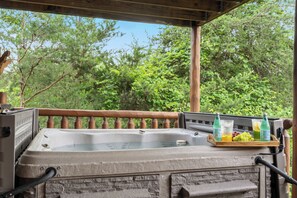 A hot tub with a wooden deck and railing, surrounded by lush greenery.