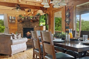 A cozy cabin interior with a stone fireplace, wooden furniture, and a large window offering a view of the outdoors.