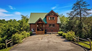 A log cabin with a green roof, a front porch, and a gravel driveway.