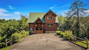 A log cabin with a green roof, a front porch, and a gravel driveway. - Charm, Warmth, Entertainment! Sleeps 10-Hot Tub-86”TV-Dollywood 9 miles;Island 6 (Pigeon Forge)