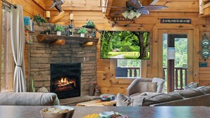 A cozy cabin interior with a stone fireplace, wooden walls, a comfortable seating area, and a television mounted on the wall.
