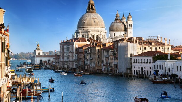 A historic Venetian canal with gondolas, a prominent domed building, and traditional architecture.