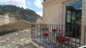 A balcony with a stone staircase, a table with red cushions, and a view of a hillside with buildings. - EXCLUSIVE AND ROMANTIC CHARME APARTMENT IN THE CORE OF HISTORIC CENTER OF MODICA (Modica)