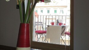 A room with a window view of a balcony, a vase with flowers, and a table with a book. - EXCLUSIVE AND ROMANTIC CHARME APARTMENT IN THE CORE OF HISTORIC CENTER OF MODICA (Modica)