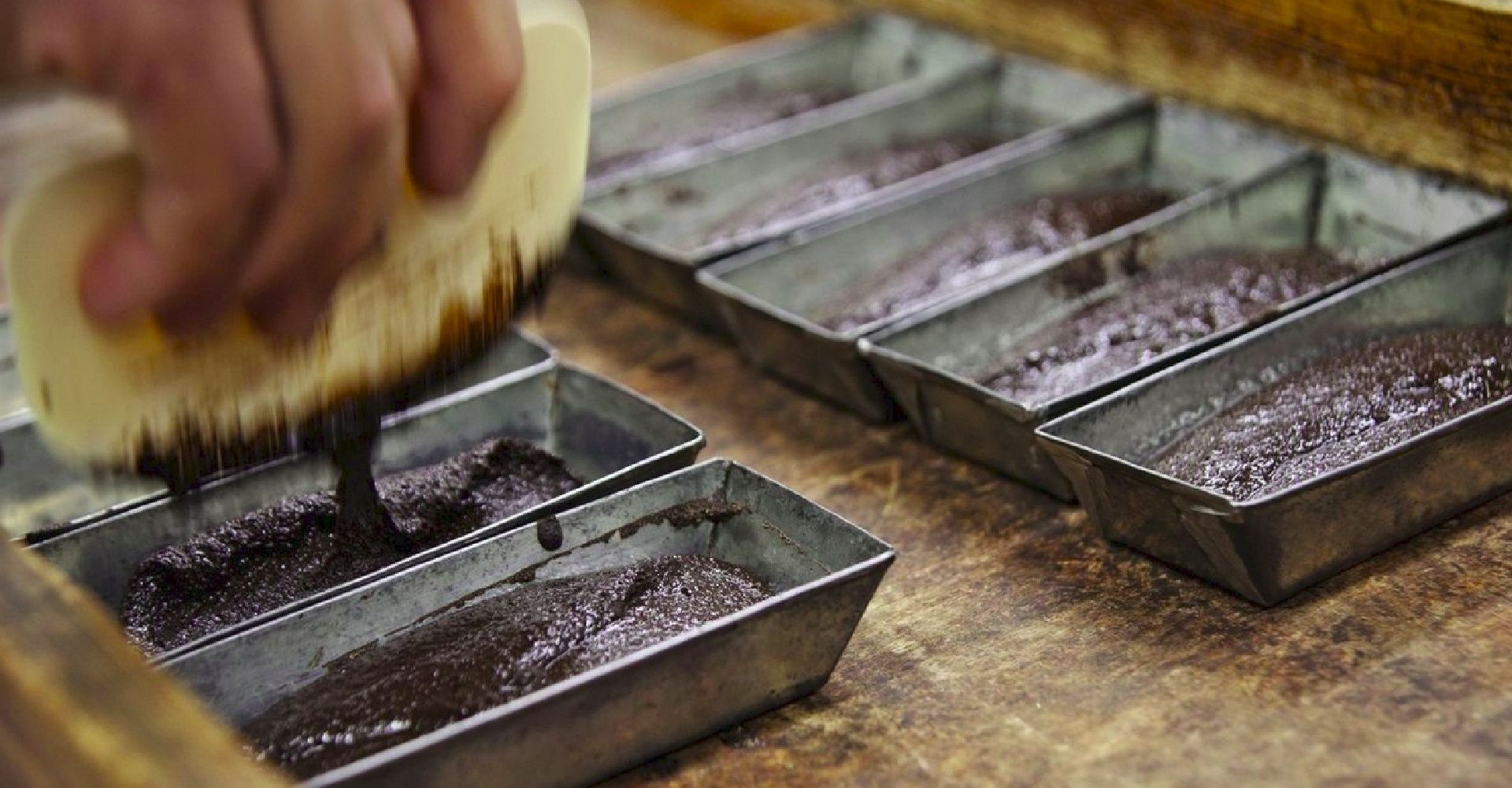 A person using a brush to apply a dark liquid to trays.