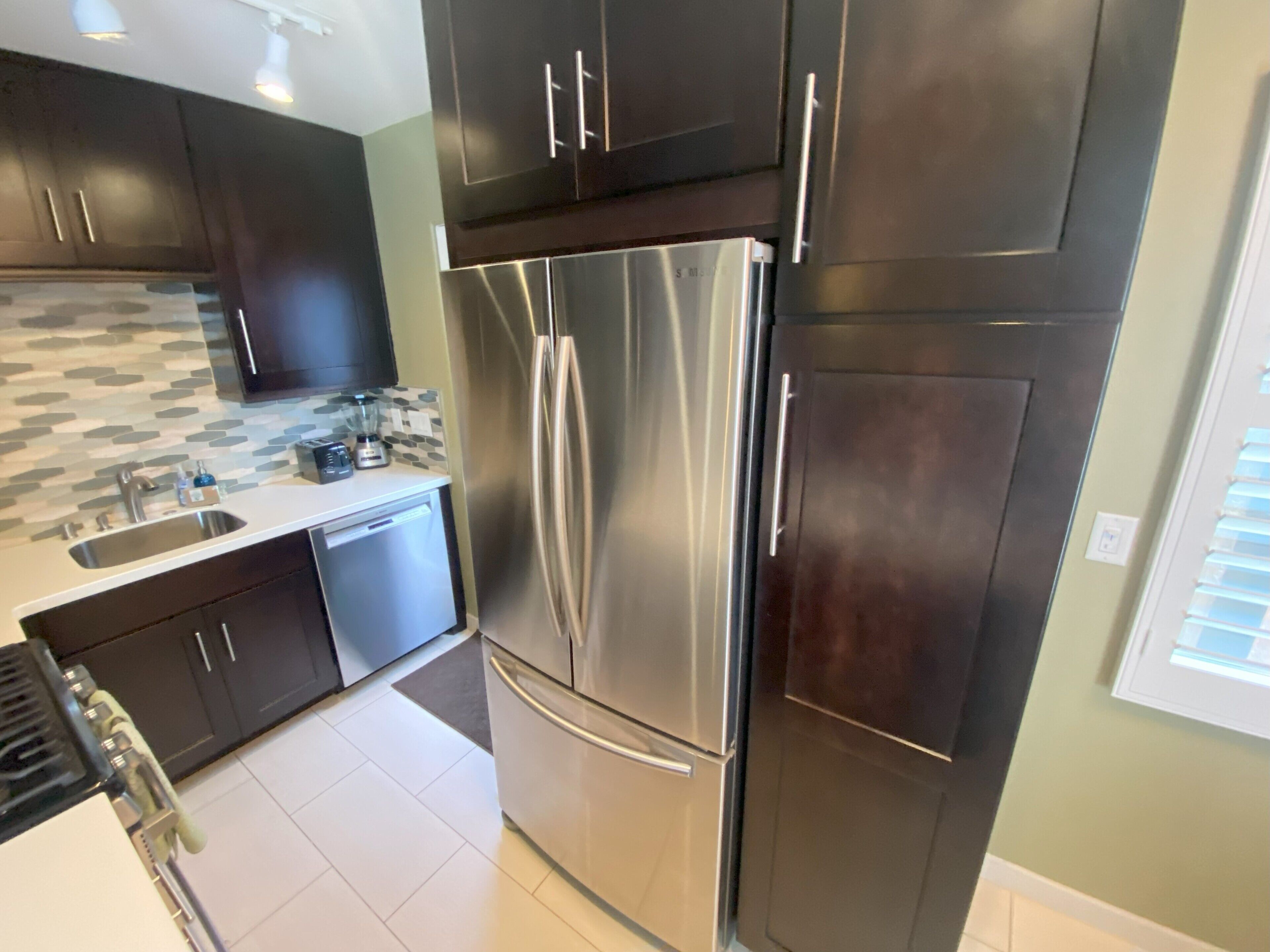 A modern kitchen with dark cabinets, stainless steel appliances, and a tiled backsplash.