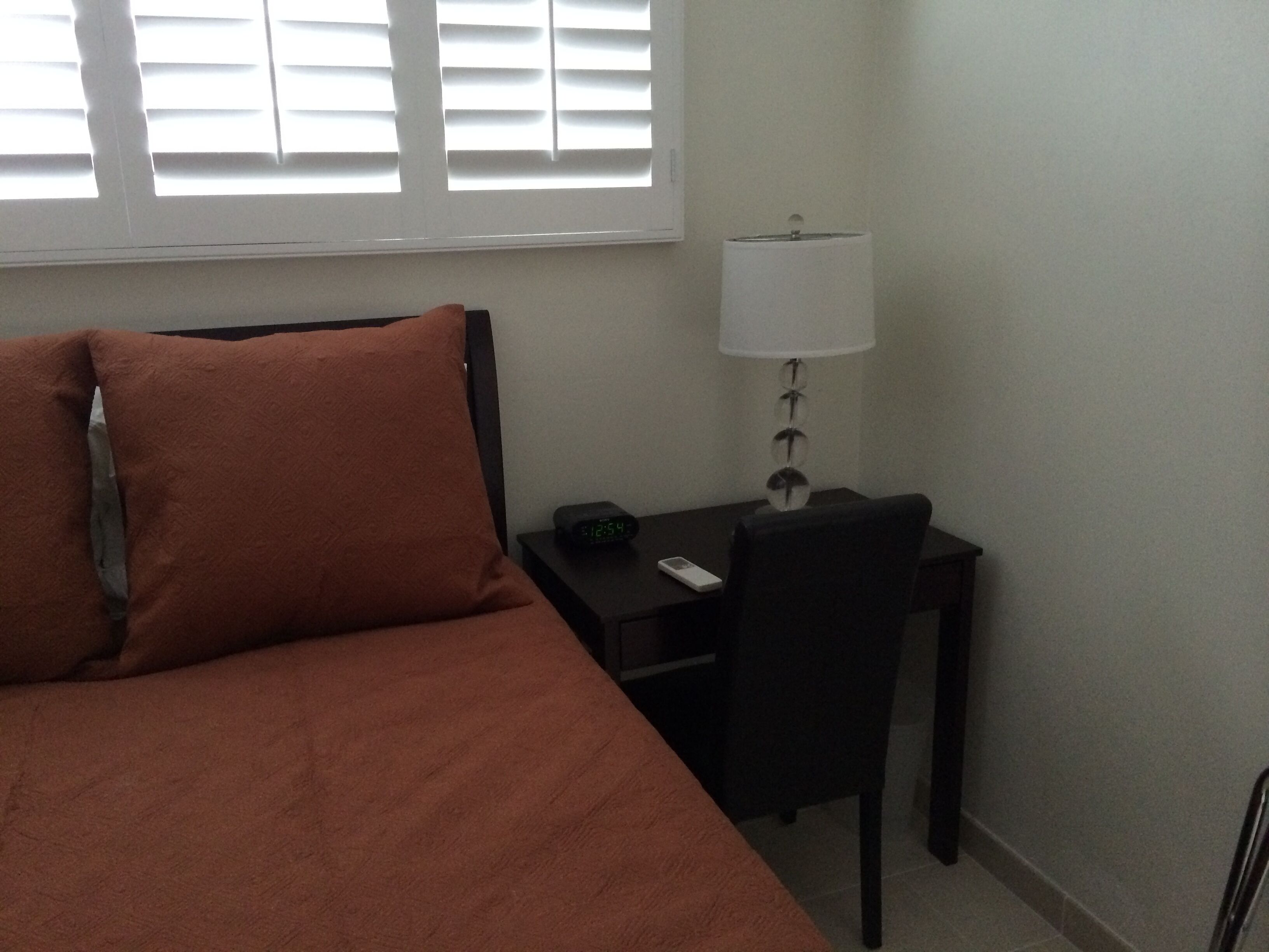 Una habitación de hotel con cama, escritorio, silla, lámpara y ventana con persianas.
