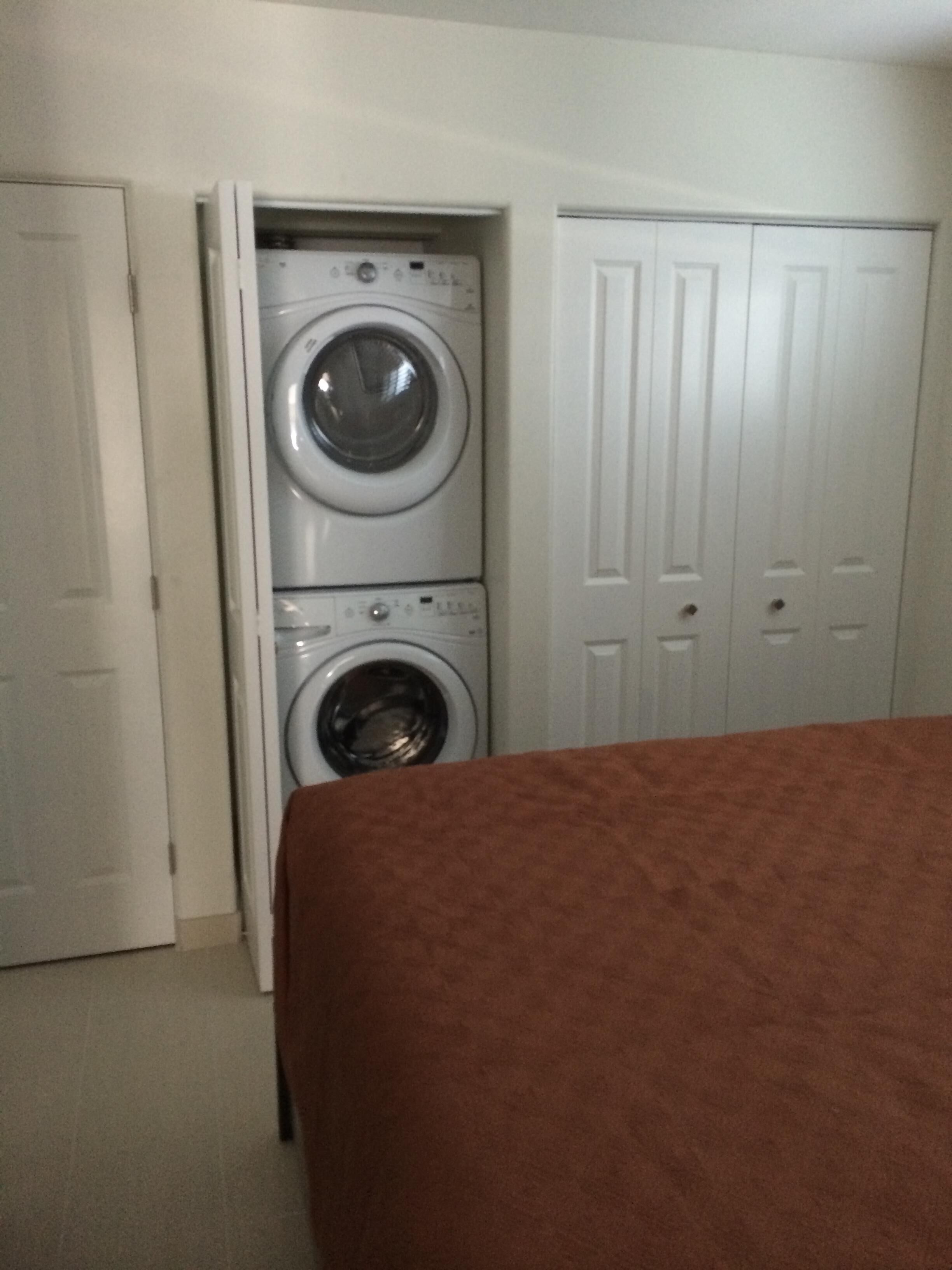 A laundry room with two stacked washers and dryers, a bed with a brown cover, and white doors.