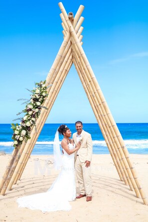 Hochzeitszeremonie mit einem Bambusbogen und floralen Dekorationen am Strand.