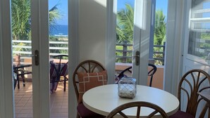 Zona de menjador amb taula rodona, cadires de vimetla i vista a l'oceà a través de portes de vidre.