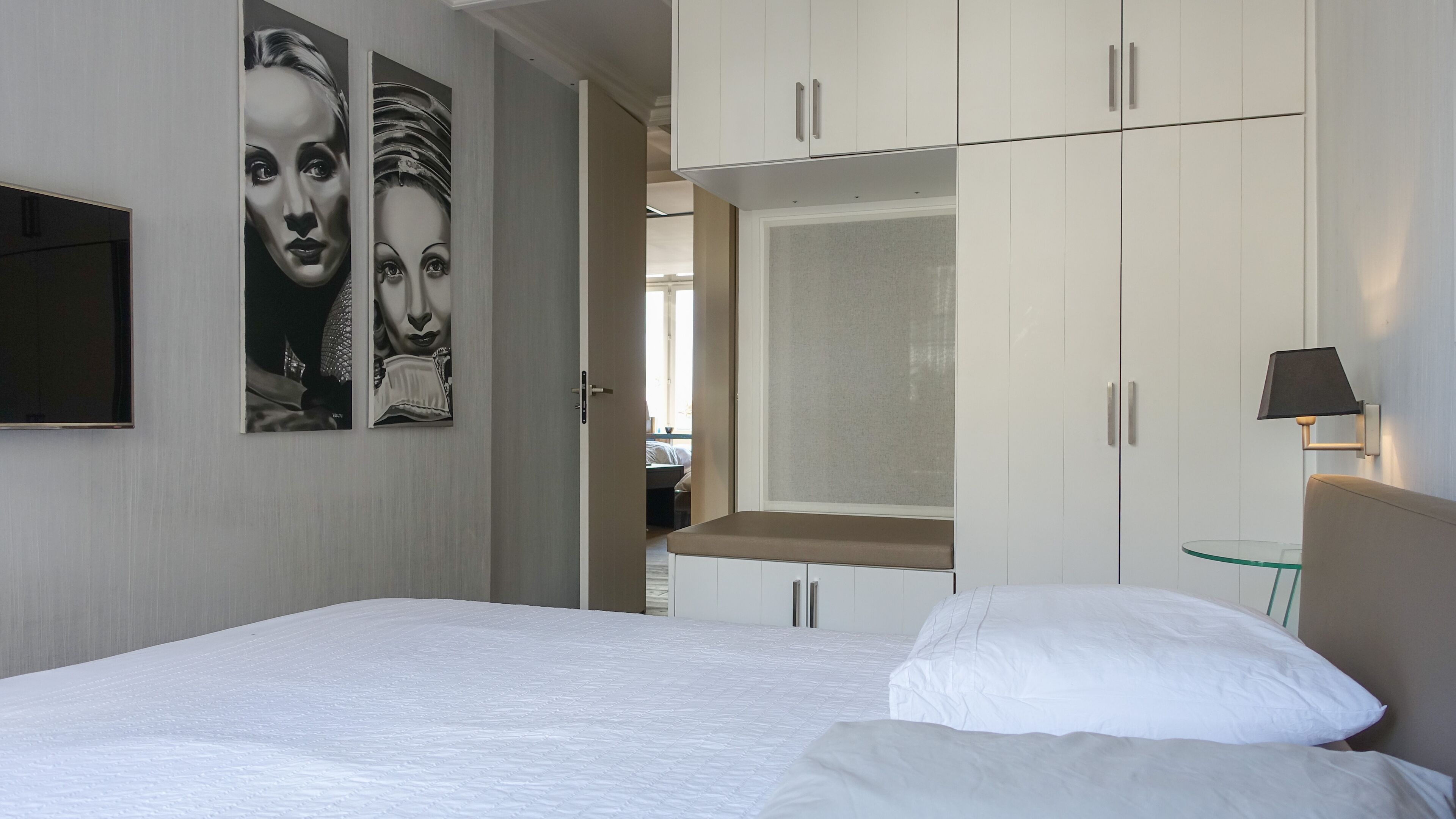 Een hotelkamer met een bed, een kledingkast, een televisie en kunst aan de muur.
