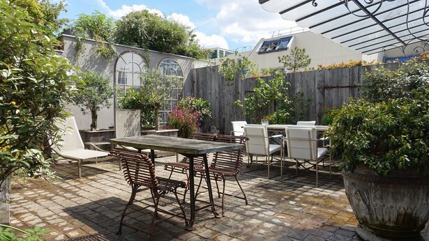 Een terras buiten met een houten tafel en stoelen, omgeven door potplanten en een houten omheining.