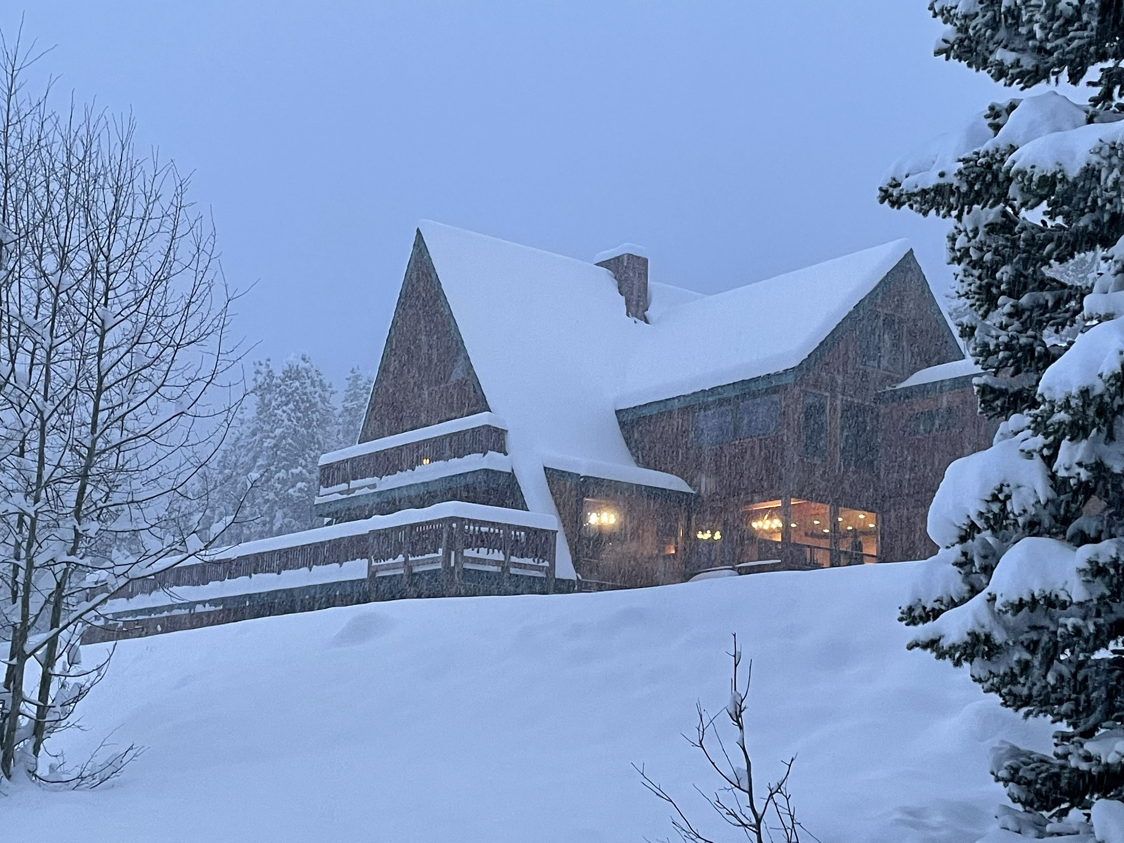 Een groot, meerhoog gebouw met een steil dak bedekt met sneeuw, omgeven door met sneeuw beladen bomen.