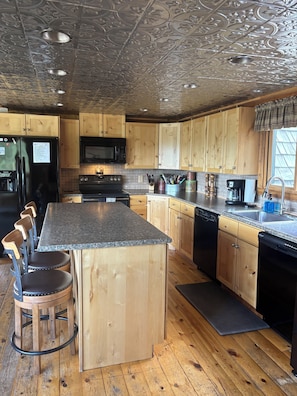 Une cuisine avec des meubles en bois, un plan de travail en granit, un réfrigérateur noir, un four à micro-ondes, une cuisinière, une machine à café et un lave-vaisselle.