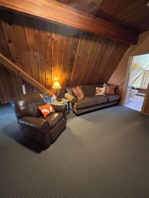 A cozy loft bedroom with a sloped ceiling, a brown leather chair, a gray sofa, and a small table with a lamp. - Specializing in Micro Weddings and Corporate Retreats. Large meeting event space (Breckenridge)