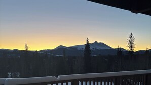Um deck coberto de neve com guarda-corpo, com vista para uma floresta e montanhas.