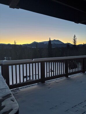 A snowy deck with a railing overlooking a forest and mountains.