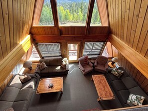 A cozy cabin interior with a sofa, armchairs, and a coffee table. Large windows offer views of a forested landscape. - Private Chef included for Breakfast and Dinners.  Meeting room, ultimate privacy (Breckenridge)