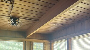 Une chambre avec un plafond en bois, un lit recouvert d’une couvre-lit à motifs floraux et des fenêtres équipées de stores.