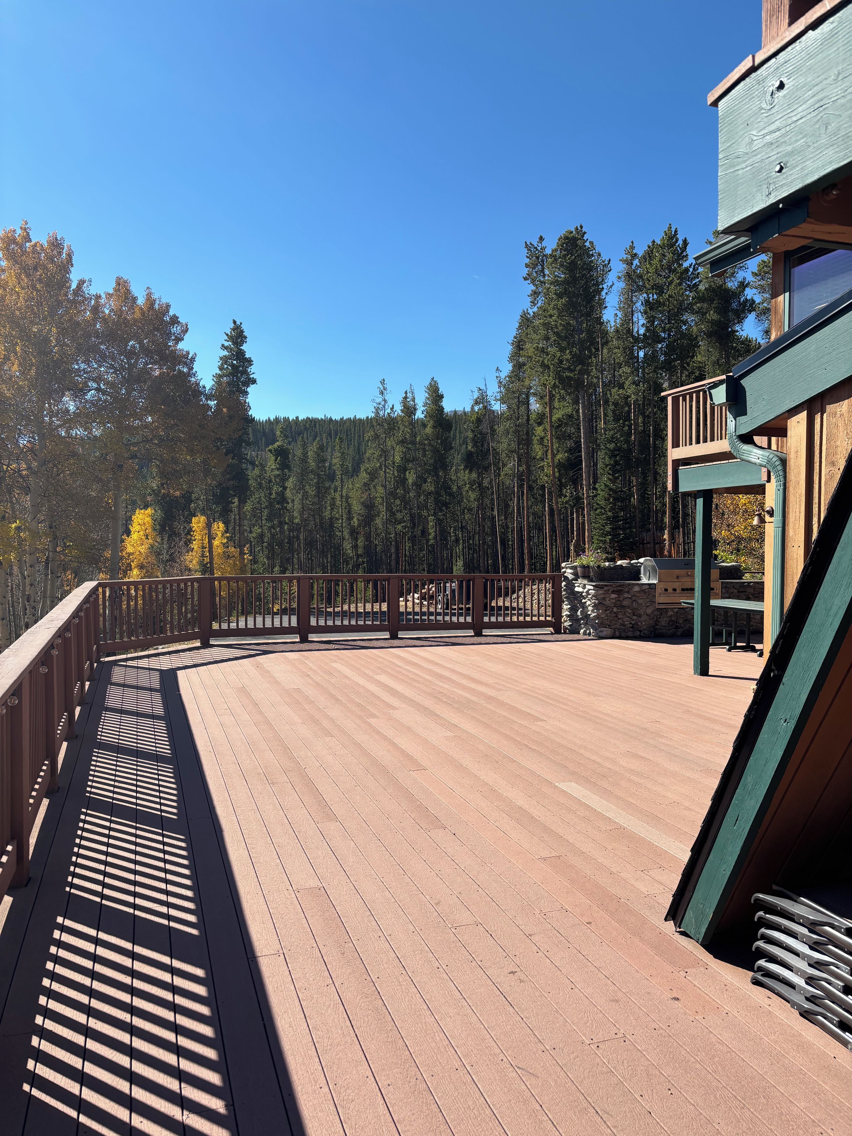 A wooden deck with a metal railing, surrounded by trees and a clear sky.