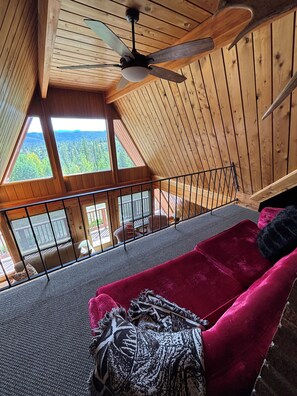 A wooden interior with a ceiling fan, a red sofa, and a view of a forest through large windows. - Specializing in Micro Weddings and Corporate Retreats. Large meeting event space (Breckenridge)