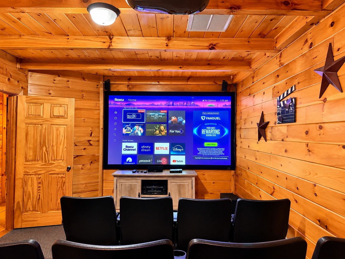 Een houten interieur met een televisie waarop het Roku Home scherm wordt weergegeven, een zithoek met stoelen, en een sterren decoratie aan de muur.