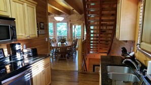 A wooden cabin interior with a kitchen, dining area, and a staircase.