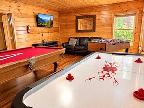 A pool table, a foosball table, a sofa, and a fireplace in a wooden room.