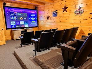 A theater room with a large screen displaying a Roku interface, wooden walls, and a sign indicating the room's purpose. - Free Daily Activities- Enjoy family time in our theater game room or hot tub (Sevierville)