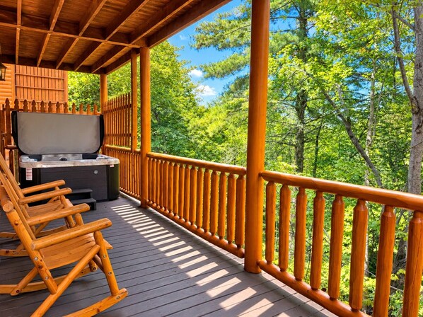 A wooden deck with a hot tub, seating, and a view of the forest. - Free Daily Activities- Enjoy family time in our theater game room or hot tub (Sevierville)