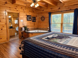 A wooden cabin bedroom with a large bed, a bathtub, and a window with curtains. - Free Daily Activities- Enjoy family time in our theater game room or hot tub (Sevierville)